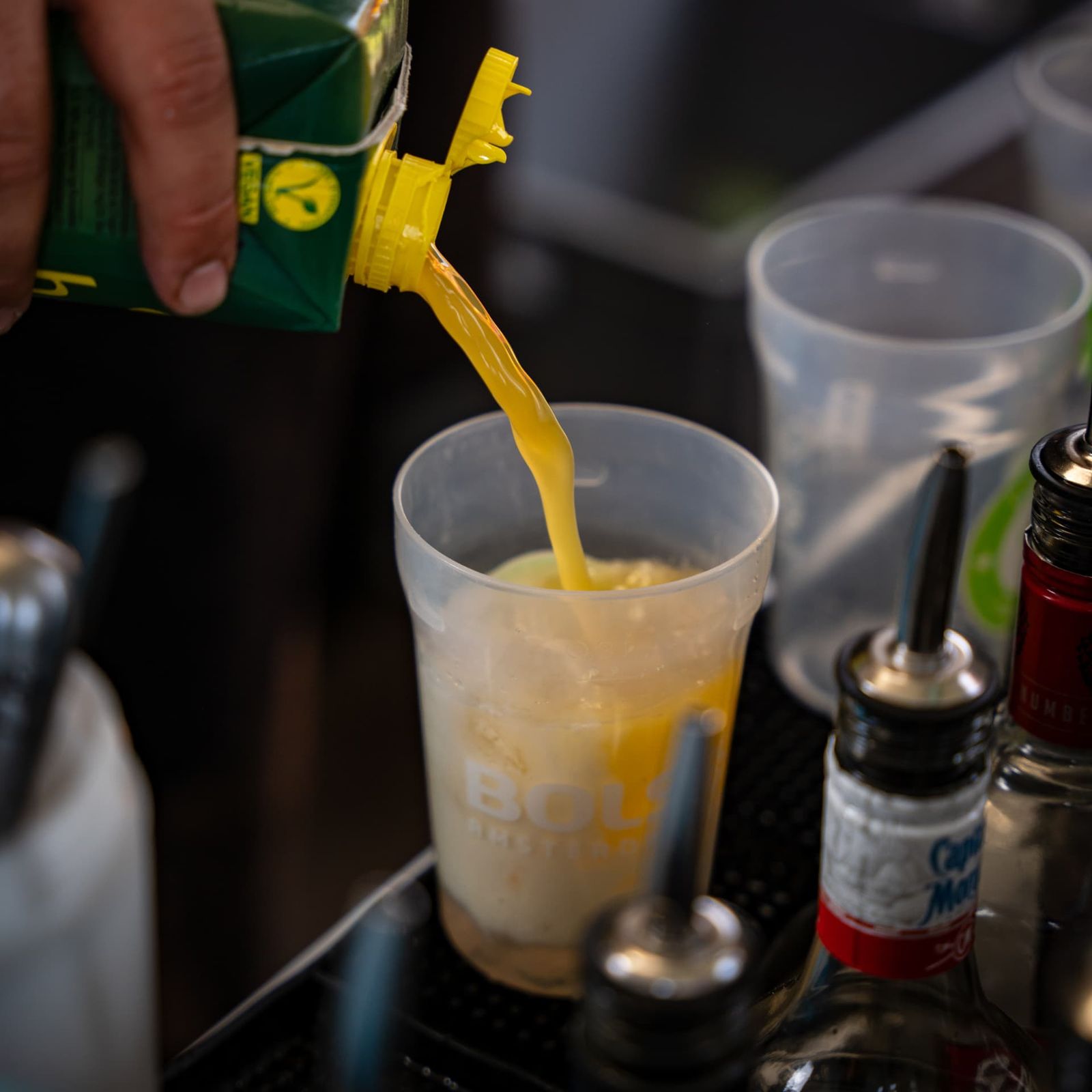 Orangensaft wird über Eis in die Cocktailbasis gegossen